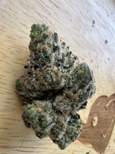 Close-up of a cannabis flower bud on a light wood surface.