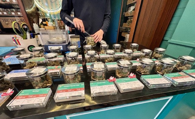 Jars of cannabis displayed on a counter, person scooping buds.