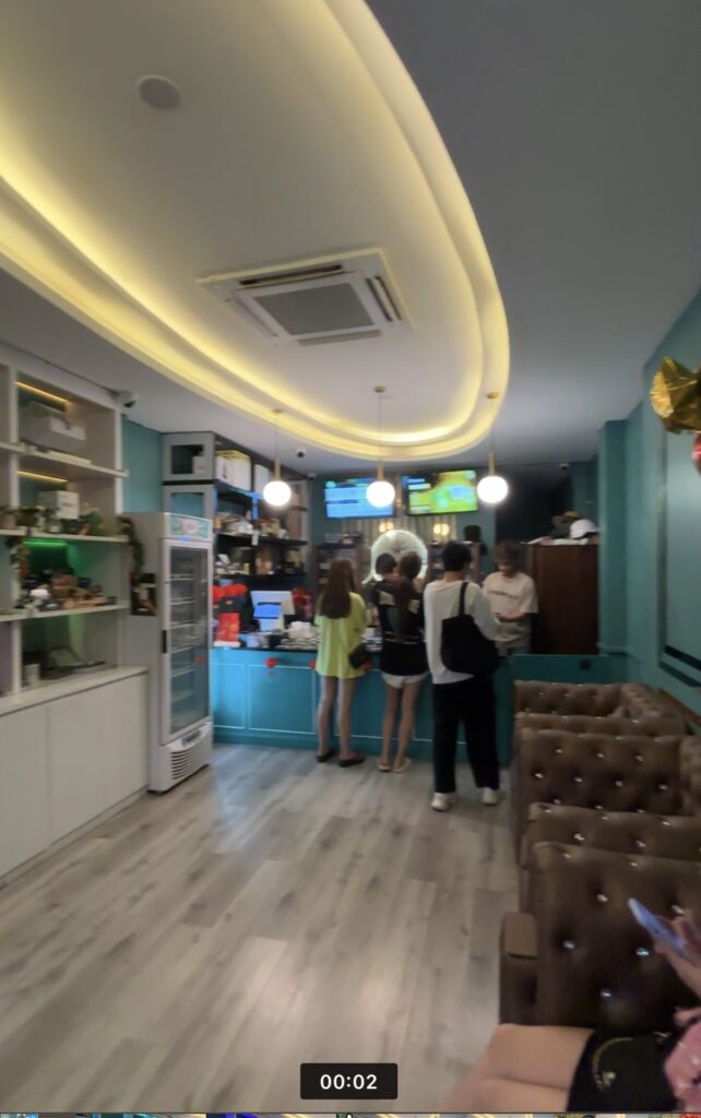 People ordering at a cafe counter with a display fridge and seating area.