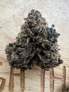 Close-up of a cannabis flower bud on a light wood surface.