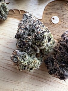 Close-up of cannabis flower buds on a light wood surface.