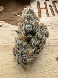 Cannabis flower bud, purple and green, covered in trichomes on wood.