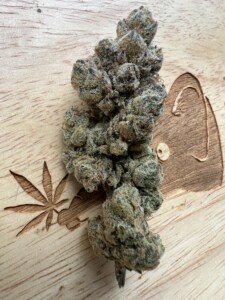 Cannabis bud on a wooden surface with leaf and dog carvings.