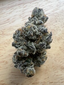 Close-up of a cannabis flower bud on a light wood surface.
