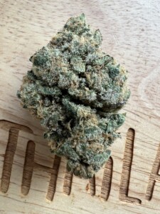 Cannabis flower bud on a light wood surface with an incised word.
