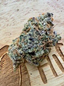Close-up of a trichome-covered cannabis flower bud on wood.