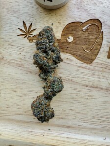 Cannabis flower bud on a wooden surface with leaf and animal carvings.