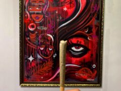 Hand holding a pre-rolled joint in front of art.