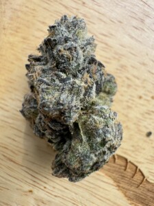 Close-up of a dense, frosted cannabis bud on a wooden surface.