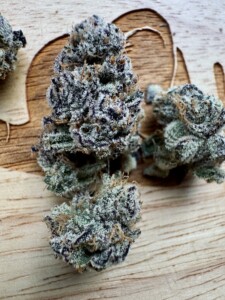Three cannabis flower buds on a wooden surface.