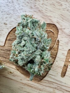 Close-up of a frosty green cannabis bud on wood.