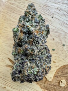 Close-up of a colorful cannabis flower bud on a wooden surface.