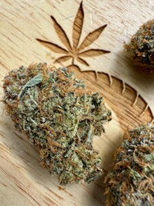 Close-up of three cannabis buds on a wooden surface with a carved marijuana leaf.