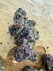 Purple and green cannabis flower bud on a wooden surface.