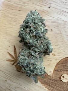 Close-up of a dense cannabis flower bud on a wooden surface.
