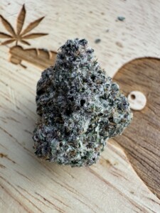 Close-up of a trichome-covered cannabis flower bud on a wooden surface.