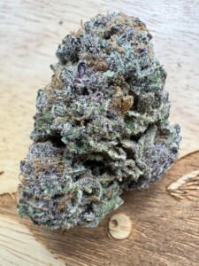 Close-up of a dense cannabis flower bud with visible trichomes on a wooden surface.