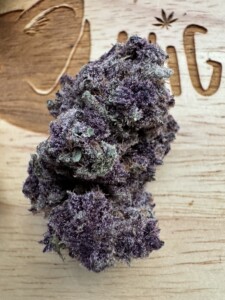Purple cannabis bud on a wooden surface.