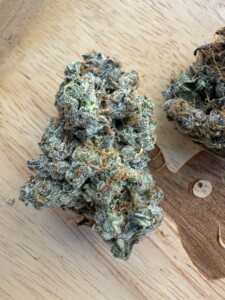 Two cannabis flower buds on a wooden surface.