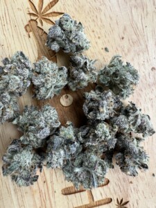 Pile of cannabis buds on a wooden surface with a carved cannabis leaf.