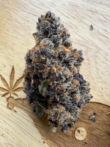 Close-up of a purple cannabis bud on a wooden surface with a cannabis leaf design.