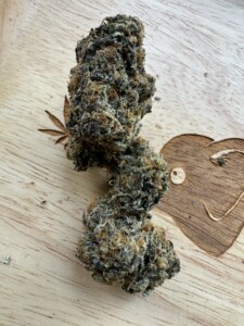 Cannabis flower bud on a wooden surface with leaf and heart carvings.