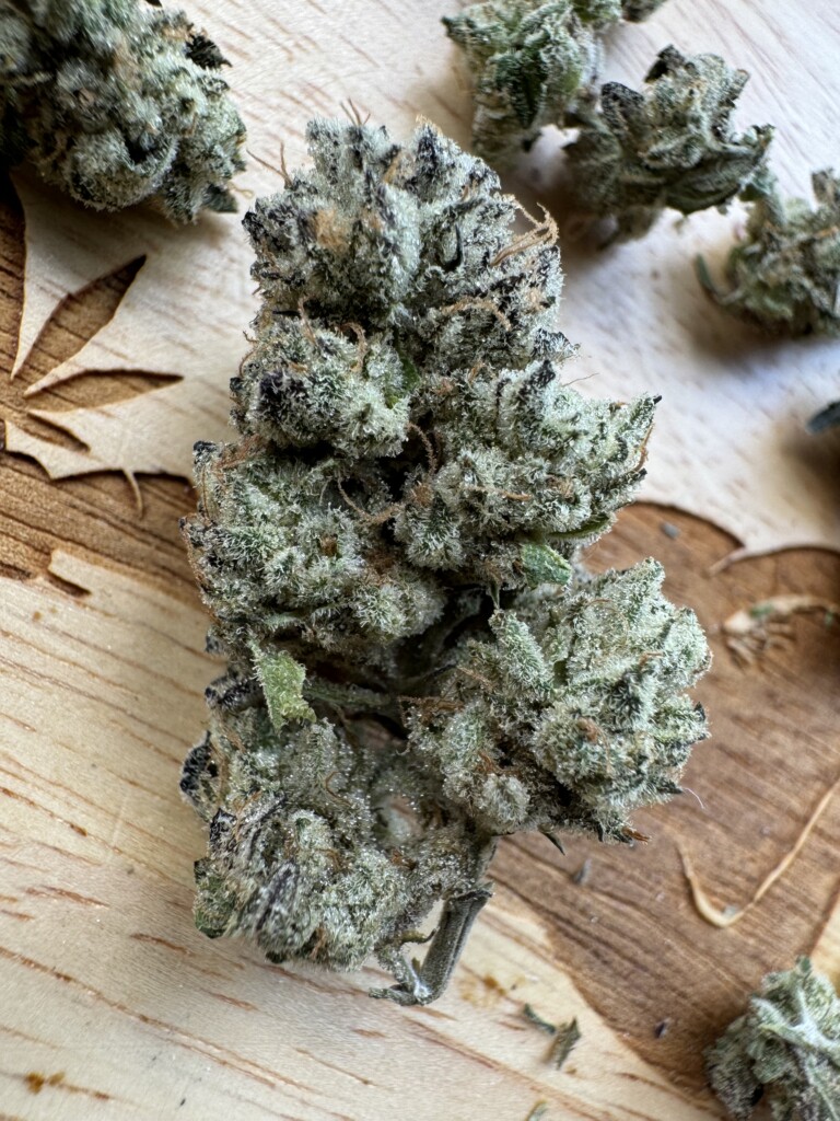 Close-up of a frosty cannabis bud on a wooden surface.