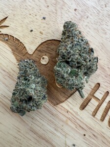 Two cannabis buds on a wooden surface with carved design.