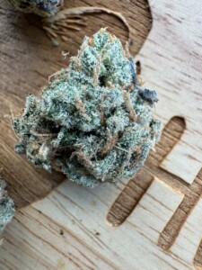 Close-up of a cannabis bud with trichomes, set on a wooden surface with a cutout design.