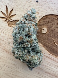 Cannabis bud covered in trichomes on a wooden surface with cannabis leaf carving.