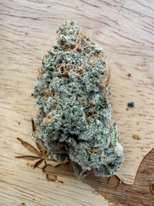 Close-up of a cannabis bud with trichomes on a wooden surface.