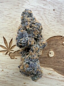 Close-up of a cannabis bud on a wooden surface with engraved designs.