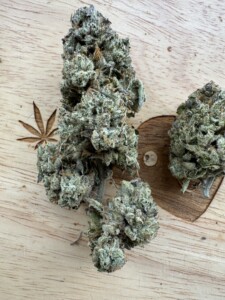 Two cannabis flower buds on a wood surface with a leaf carving.