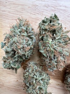 Three cannabis buds, tightly packed with trichomes and pistils, resting on a wooden surface.