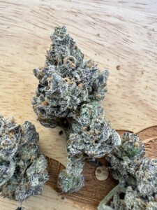 Cannabis buds with trichomes and orange hairs on a wooden surface.