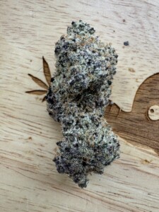 Cannabis bud with purple and green hues on a wooden surface with a leaf design.