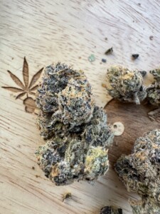 Cannabis buds on a wooden surface with a carved cannabis leaf design.