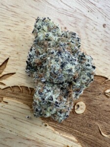 Close-up of a cannabis bud with green, black and brown coloring, on a wooden surface.