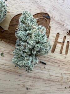 Bud of cannabis, light green with trichomes, on a wooden surface, next to a carved 