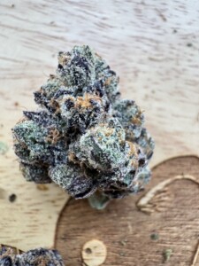 A cannabis bud with green, purple, and orange hues on a wooden surface.