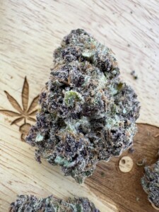 Purple and green cannabis bud with trichomes on a wood surface, etched with a cannabis leaf.