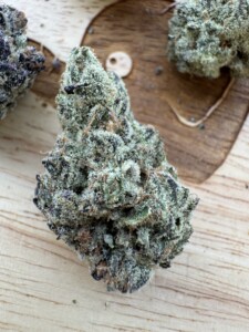 Close-up of cannabis bud with trichomes, on a wooden surface.