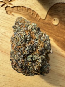Cannabis bud on a wooden surface, with details of green, purple, and orange hairs visible.