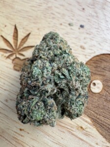 Bud of cannabis on a wooden surface, with a carved cannabis leaf and a small decorative circular wooden piece.
