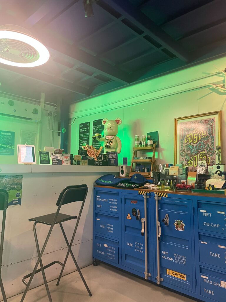 Interior of a cannabis shop with green lighting, blue storage cabinets, and a display counter with product samples, and a bear statue.