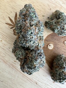 Buds of cannabis on a wooden surface with a cannabis leaf imprint.