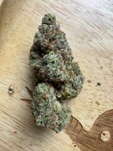 Bud of cannabis, green and brown, on a wooden tray with a decorative cutout.