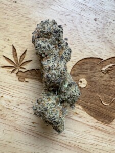 Cannabis flower bud on a wooden surface, with etched marijuana leaf and smiley face details.