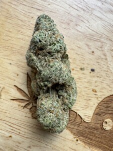 A large cannabis bud on a wooden surface with carved leaf and other design elements.
