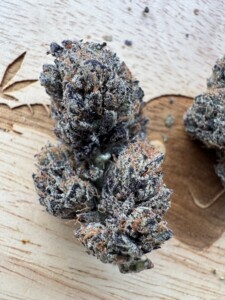 Cannabis bud with purple and orange hairs on a wooden surface.